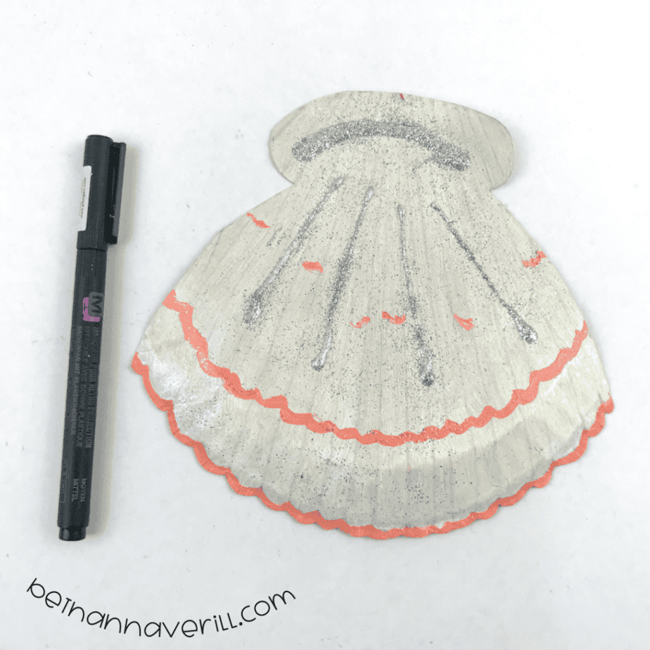 Clam shell with glitter lines next to a black marker