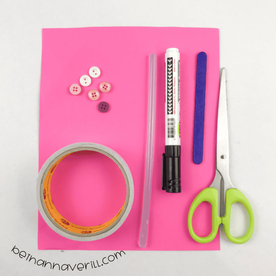 Pink construction paper, buttons, double-sided tape, a craft stick, a marker and scissors