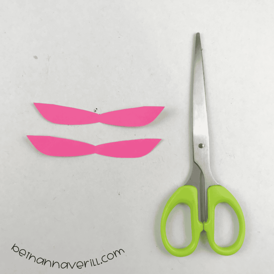 Two pink paper dragonfly wings cut out next to scissors