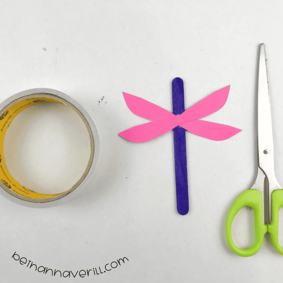 Pink paper wings taped across a purple craft stick