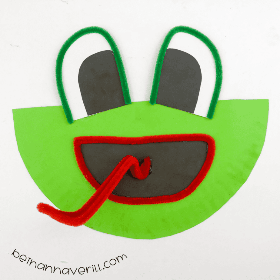 Finished paper plate frog craft with green fuzzy wire eyes and a curly red tongue