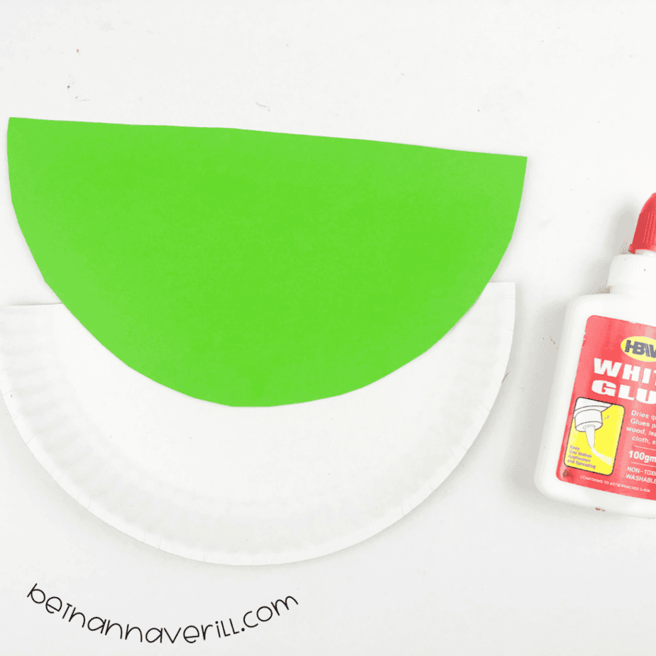 Green paper half circle being glued onto the paper plate half