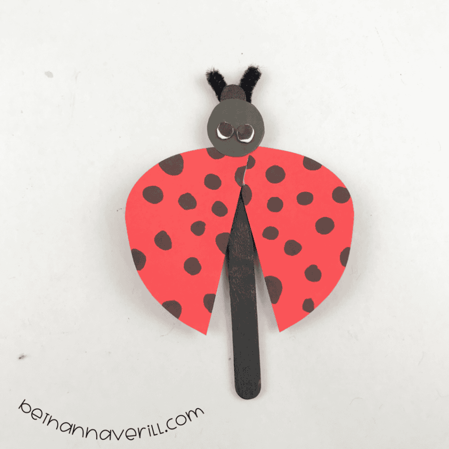 Finished popsicle stick ladybug puppet with dotted red wings and fuzzy wire antennae