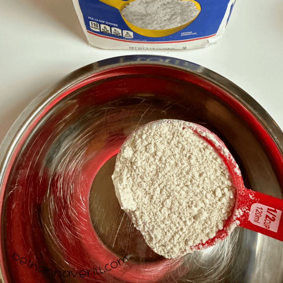 Measuring cup of flour added to a metal mixing bowl for oatmeal playdough