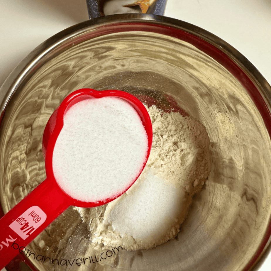 Measuring cup of salt poured over flour in a mixing bowl