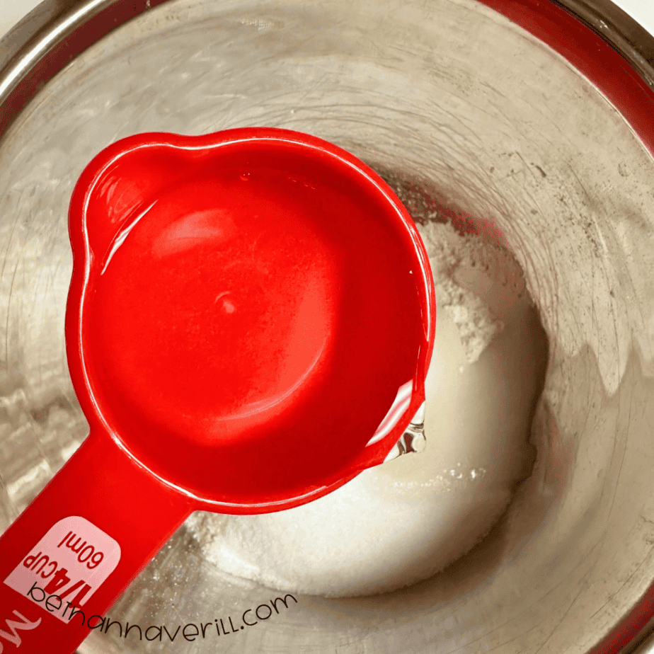 Water poured from a red measuring cup into the flour and salt