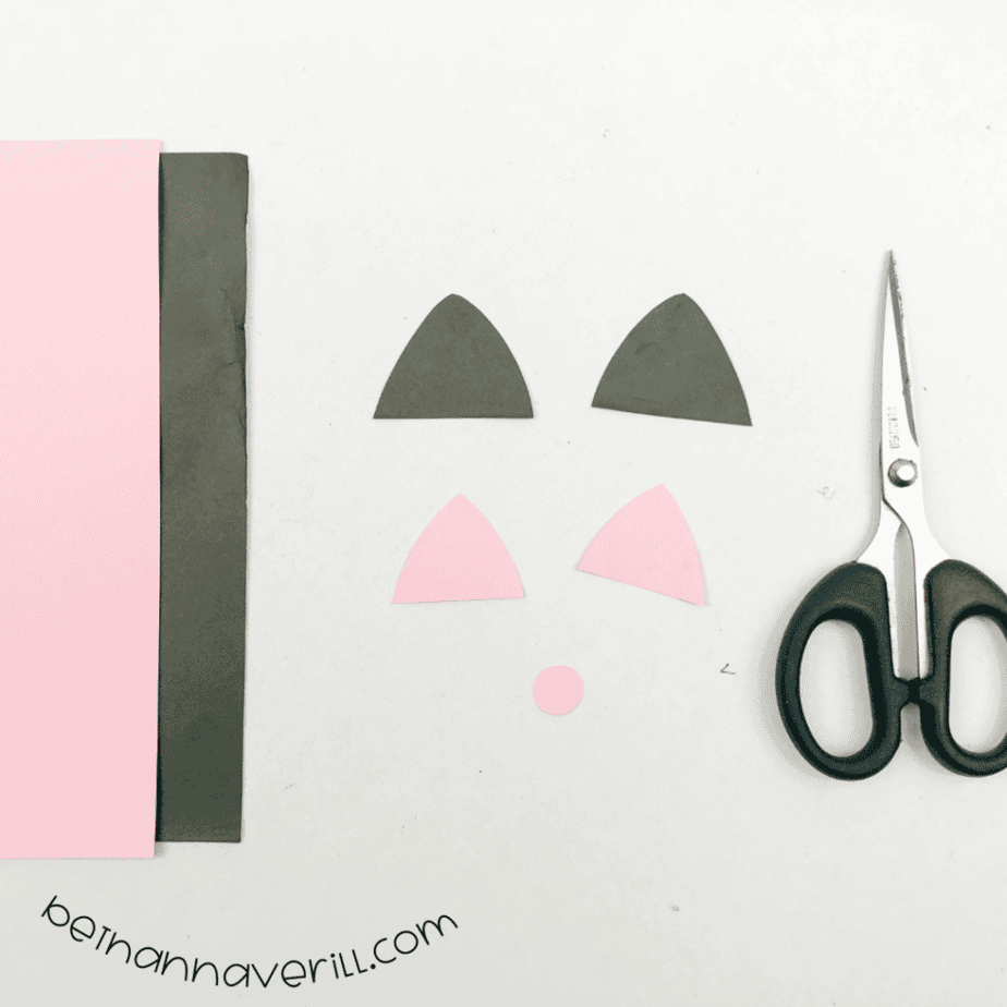 Black and pink paper cat ears and a pink nose cut out next to scissors