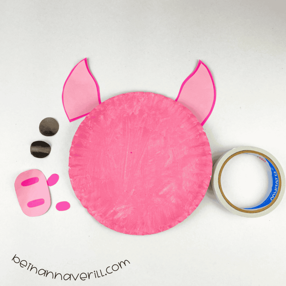Pink pig plate with ears attached behind it and the face pieces beside it