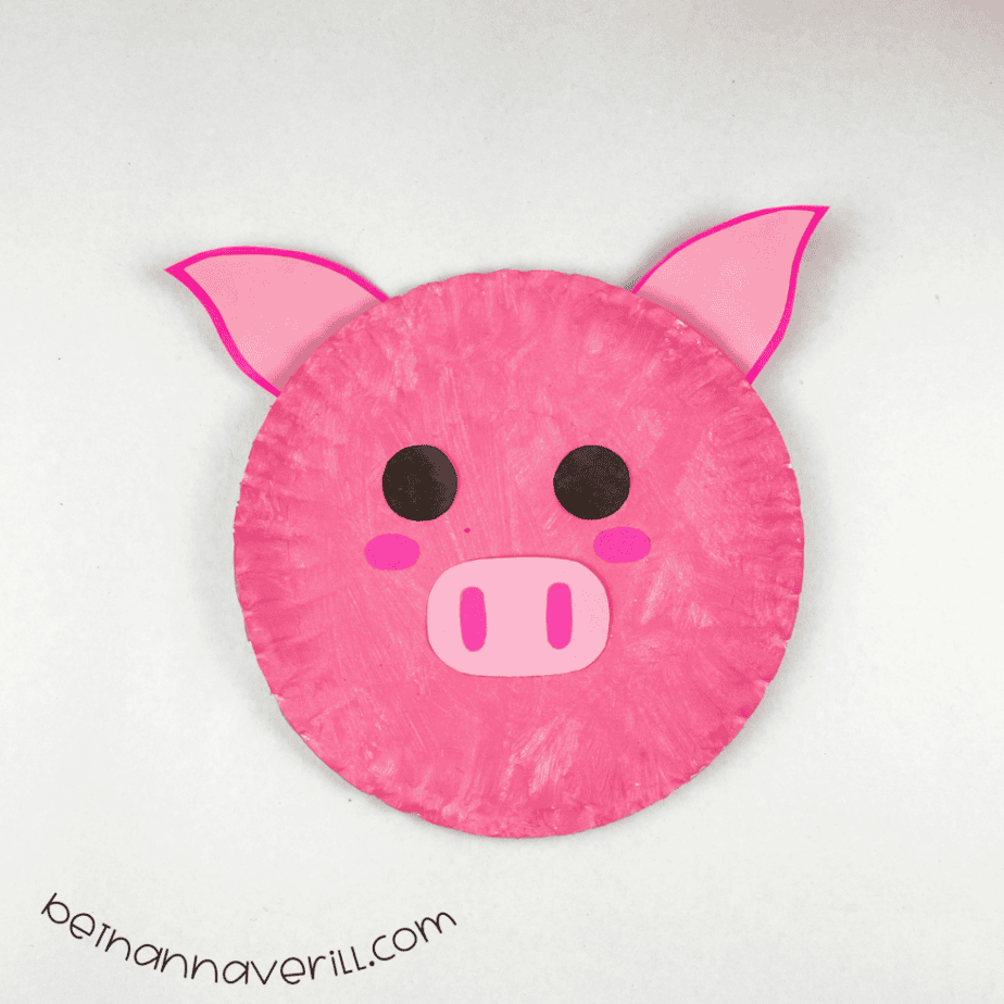 Finished pink paper plate pig craft with a snout and pointy ears