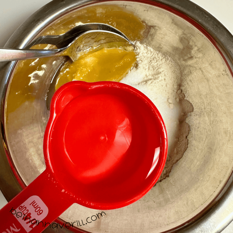 Water poured from a red measuring cup into the applesauce mixture