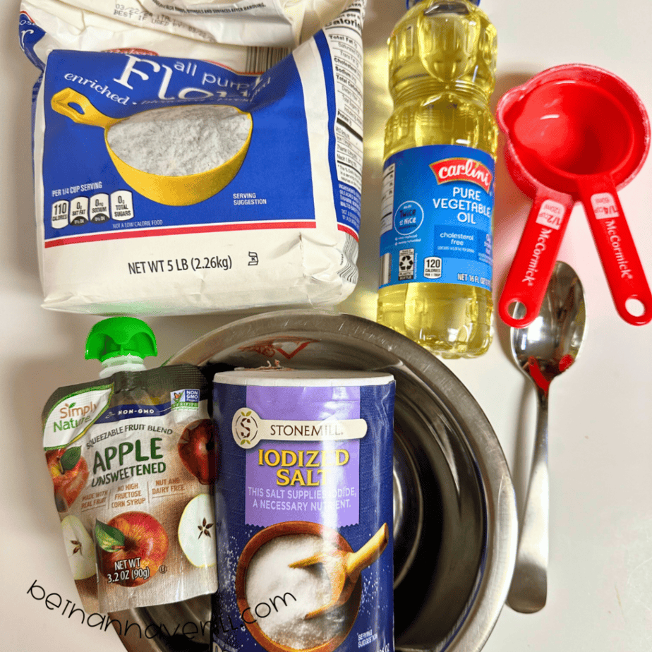 Apple playdough supplies including flour, salt, vegetable oil, an applesauce pouch, and measuring cups