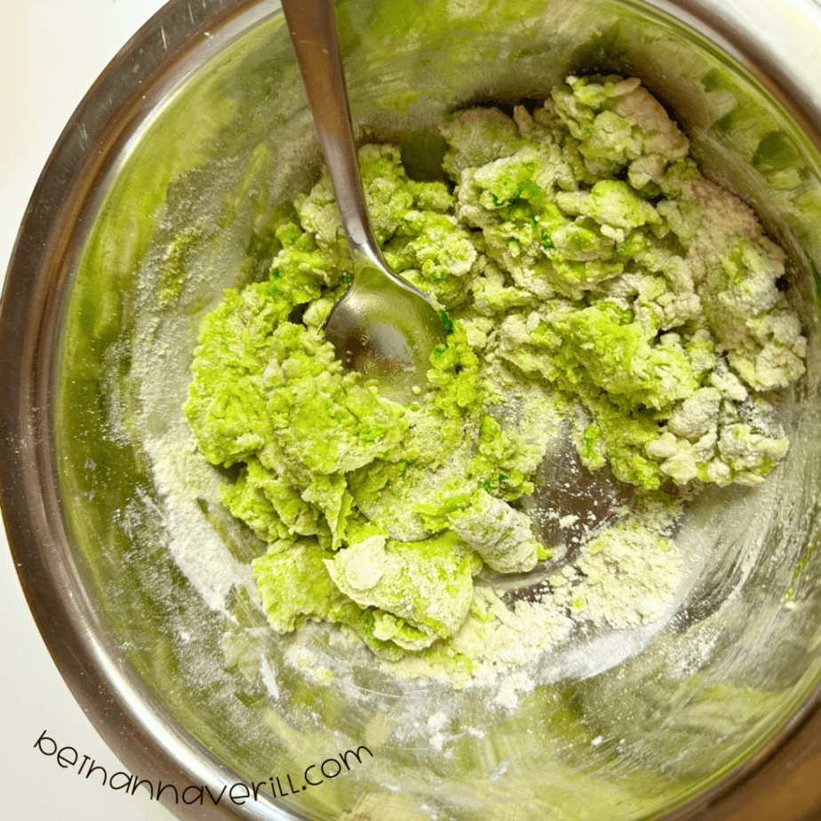 Green apple playdough mixed together in a metal bowl with a spoon