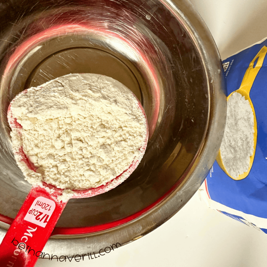 Measuring cup of flour added to a metal mixing bowl for chamomile tea playdough