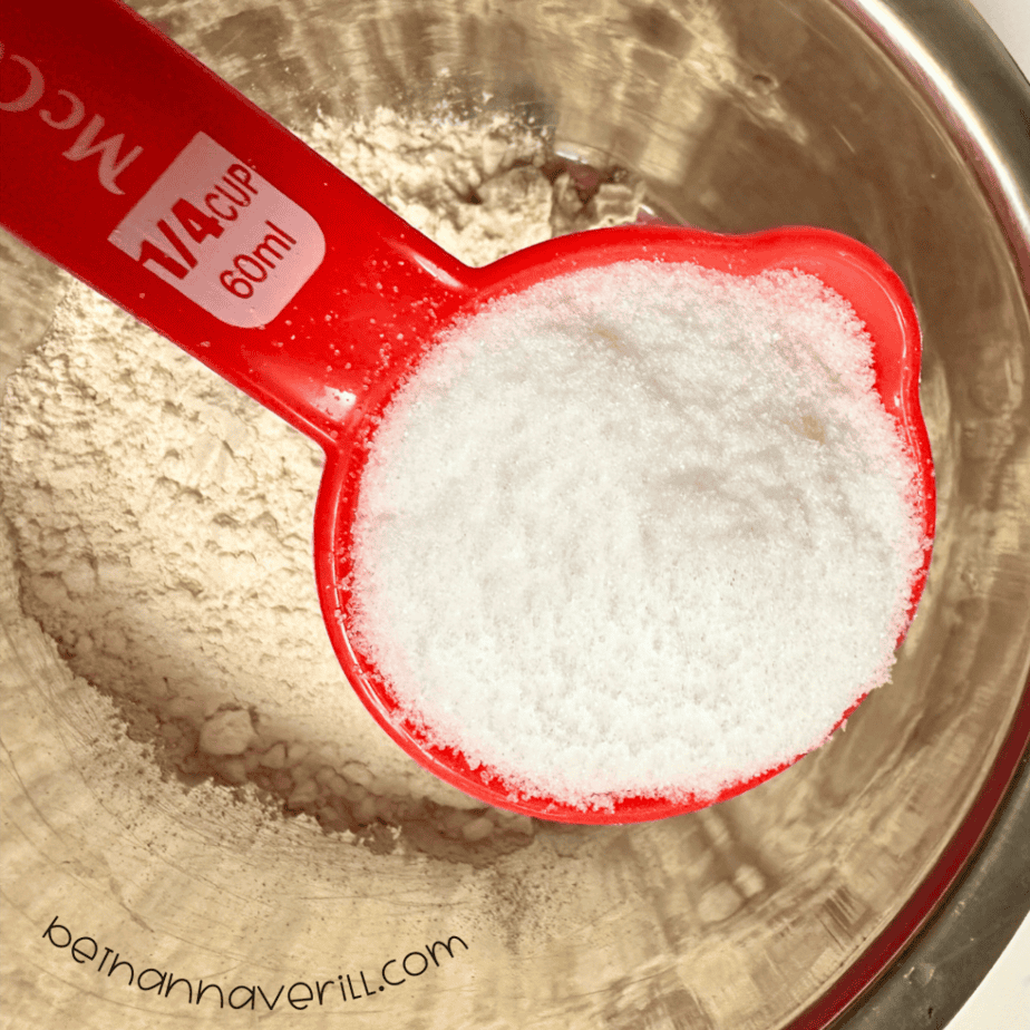 Measuring cup of salt poured over flour in a mixing bowl