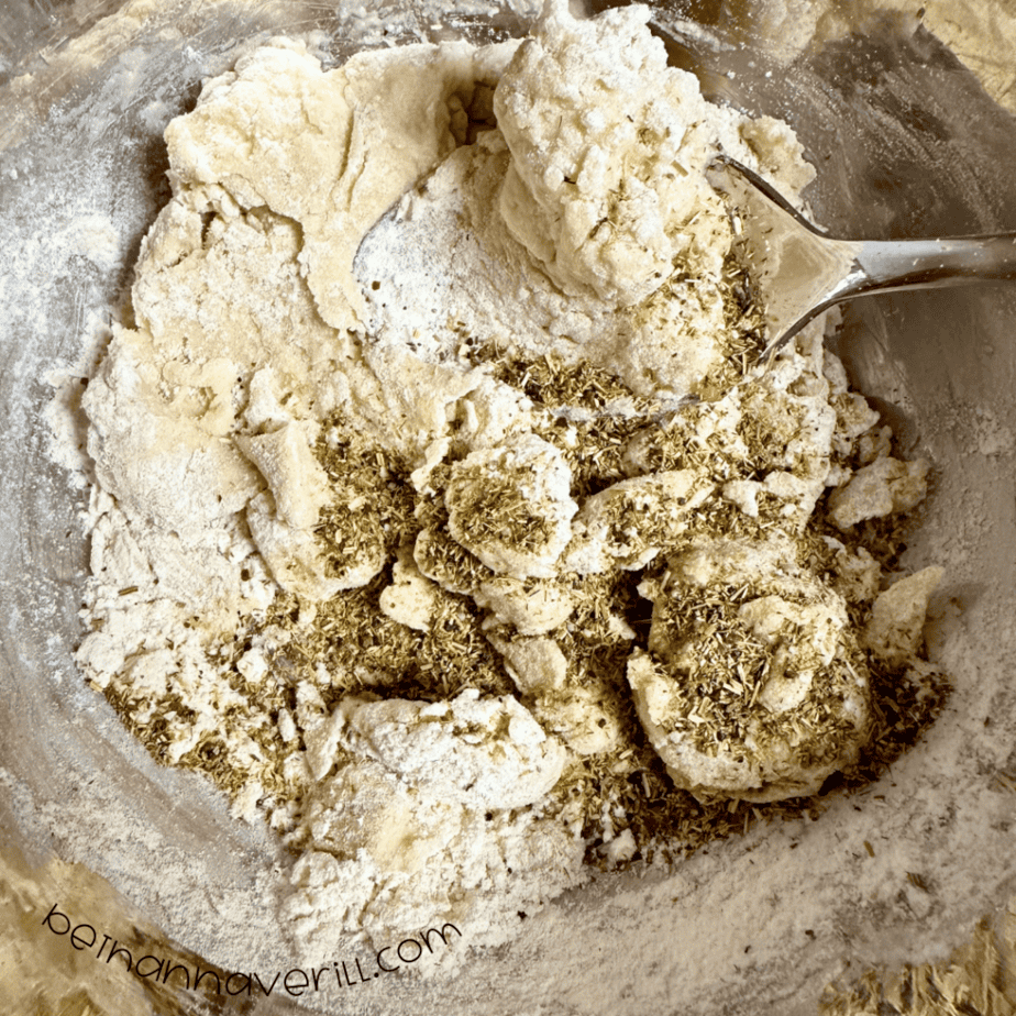 Chamomile flowers sprinkled into crumbly playdough in a metal mixing bowl