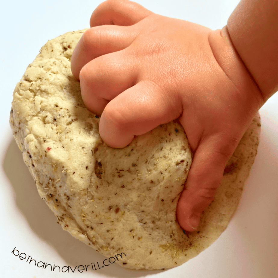 Child’s hand pressing into a ball of speckled chamomile tea playdough