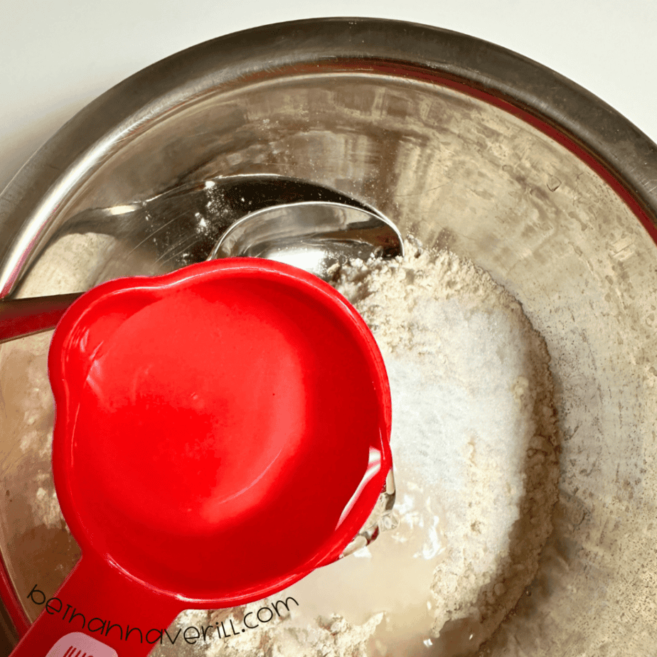 Water poured from a red measuring cup into the playdough mixture