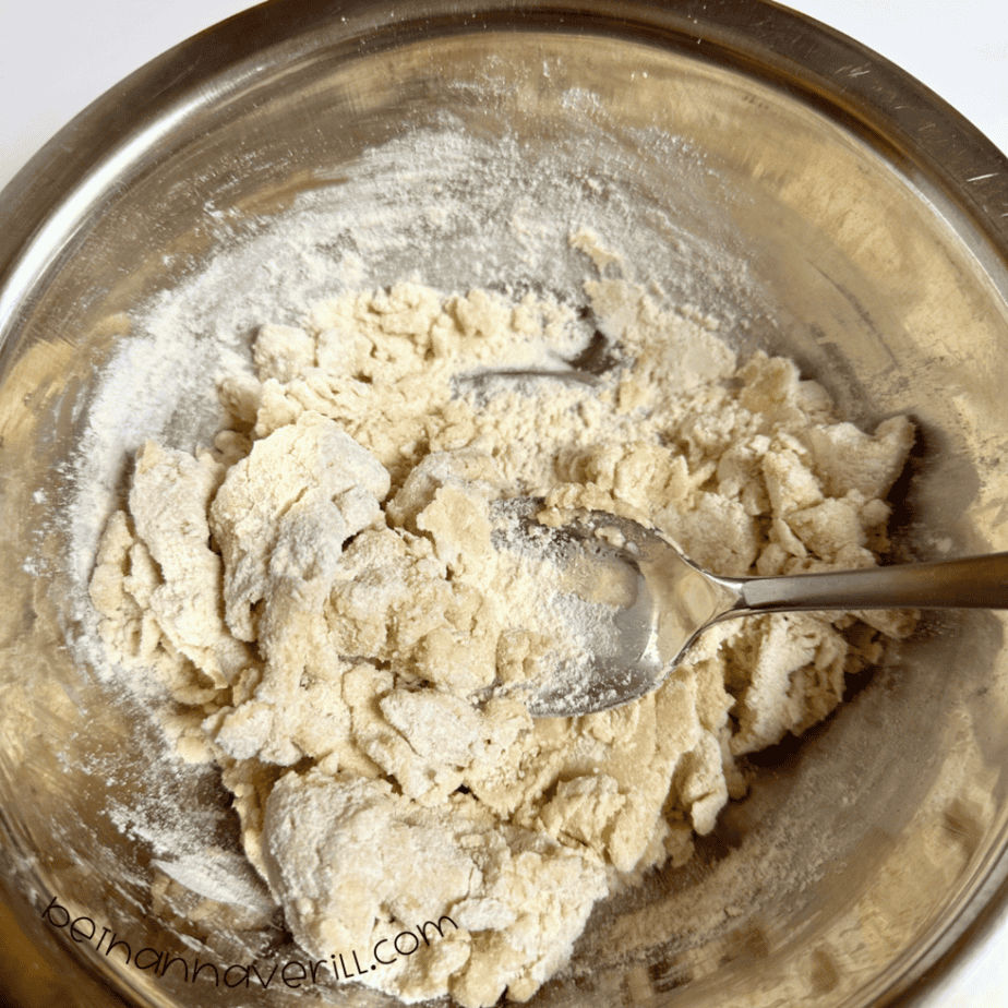 Vanilla playdough coming together in a metal mixing bowl with a spoon