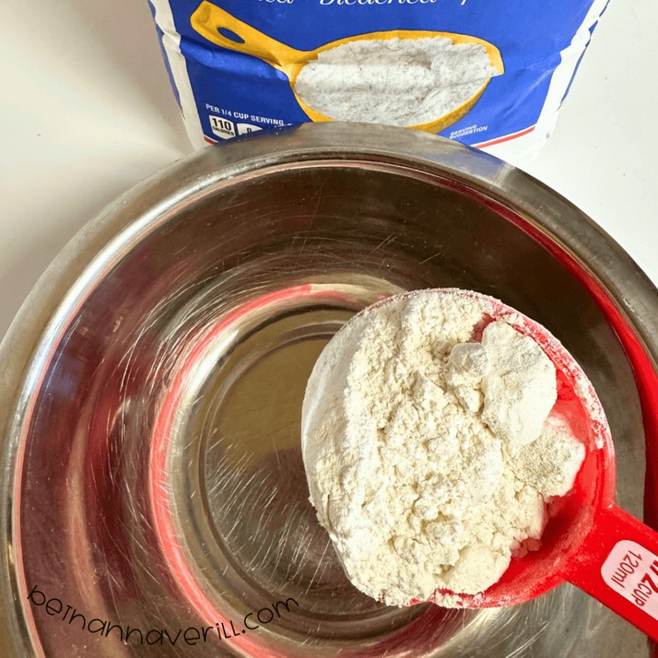 Measuring cup of flour added to a metal mixing bowl for green tea playdough