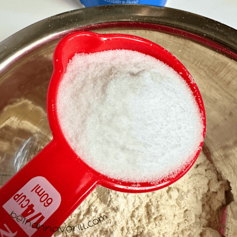 Measuring cup of salt poured over flour in a mixing bowl