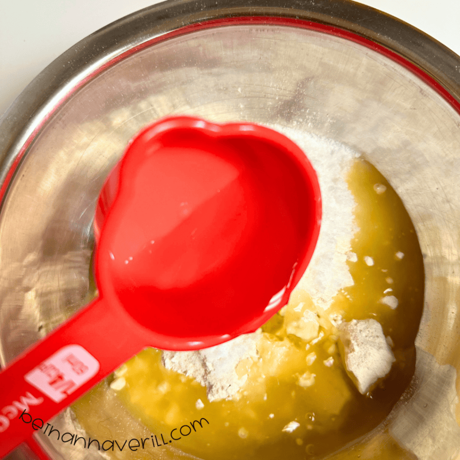 Warm green tea poured from a red measuring cup into the flour and salt