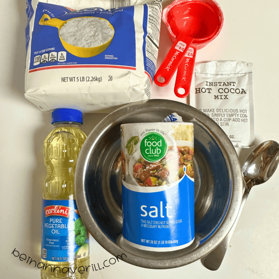 Hot cocoa playdough supplies including flour, salt, vegetable oil, a hot cocoa packet, and measuring cups