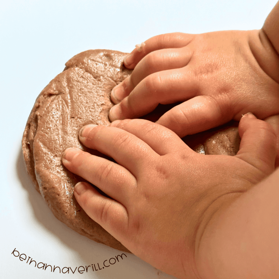 Child’s hands pressing a smooth ball of brown hot cocoa playdough