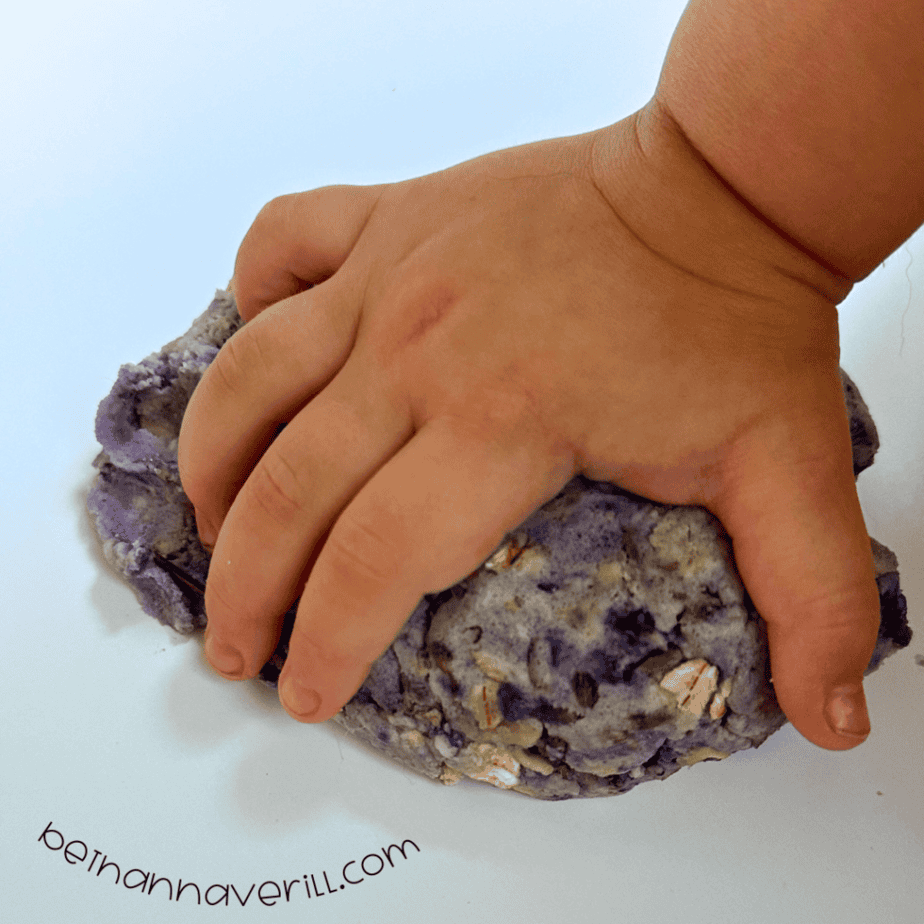 Child’s hand squeezing a ball of purple lavender oatmeal playdough