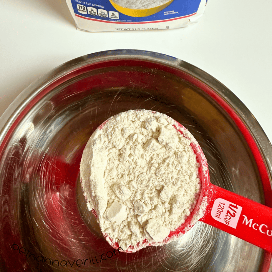 Measuring cup of flour added to a metal mixing bowl