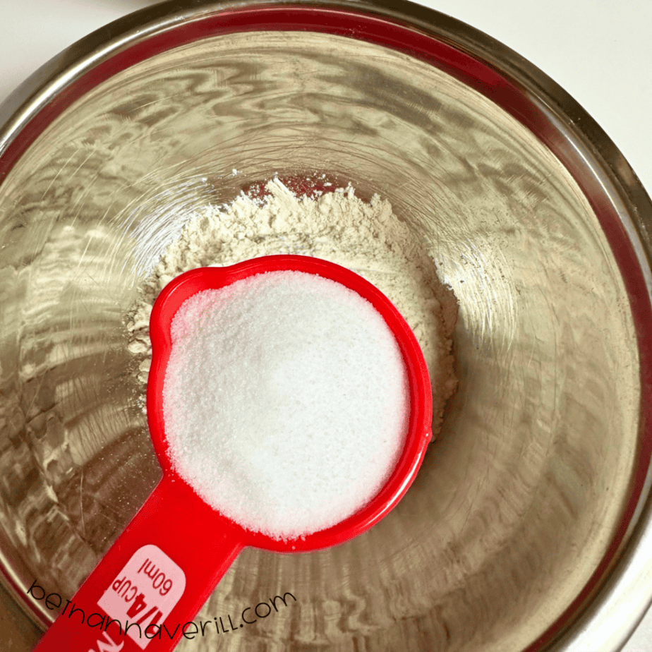 Measuring cup of salt added to the flour in a mixing bowl