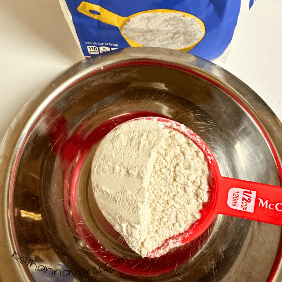 Measuring cup of flour added to a metal mixing bowl for peppermint tea playdough