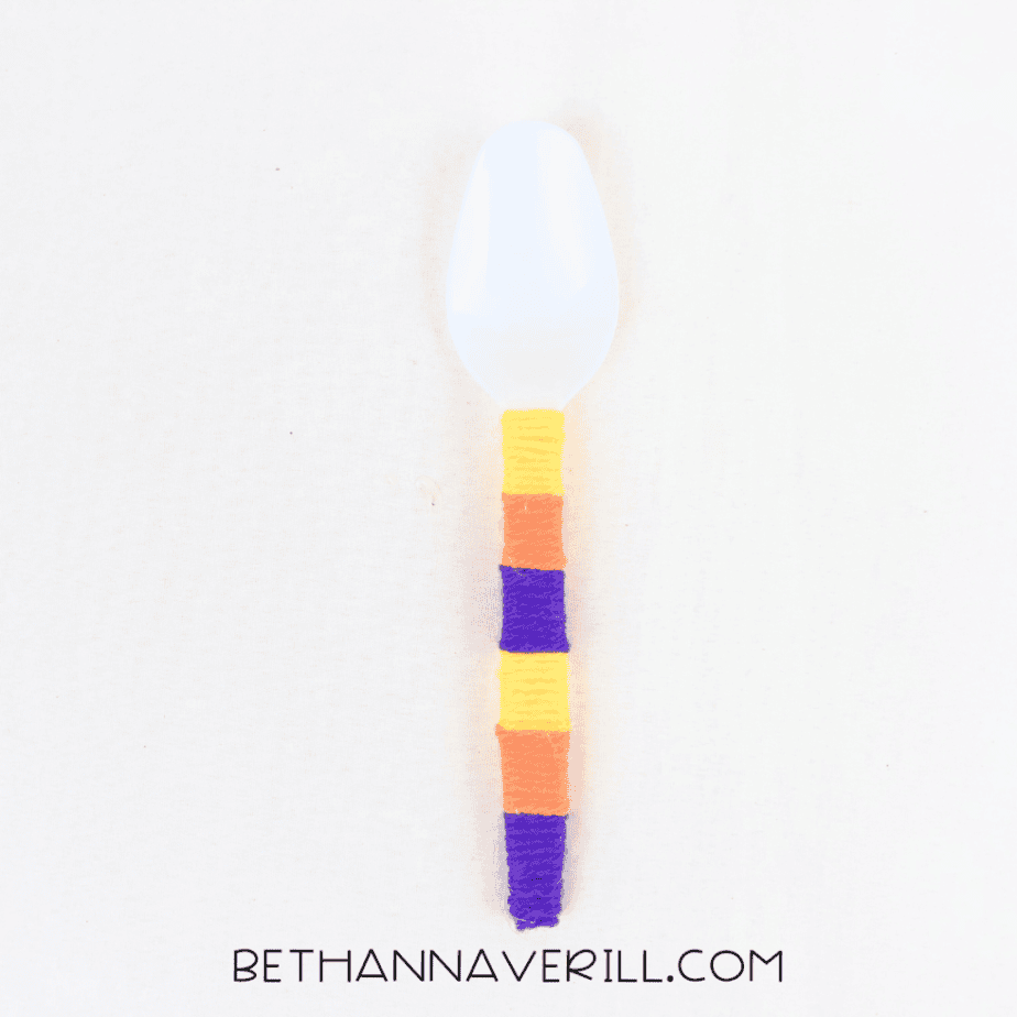 Plastic spoon handle wrapped in purple, orange and yellow yarn
