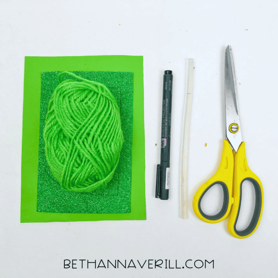Shamrock garland supplies: green paper, green yarn, pencil and scissors