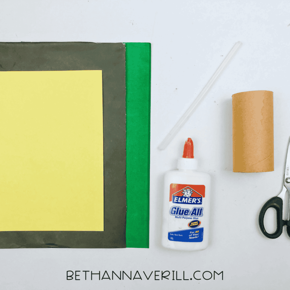 Toilet paper roll hat supplies: green, black and yellow paper, glue, scissors and a cardboard tube