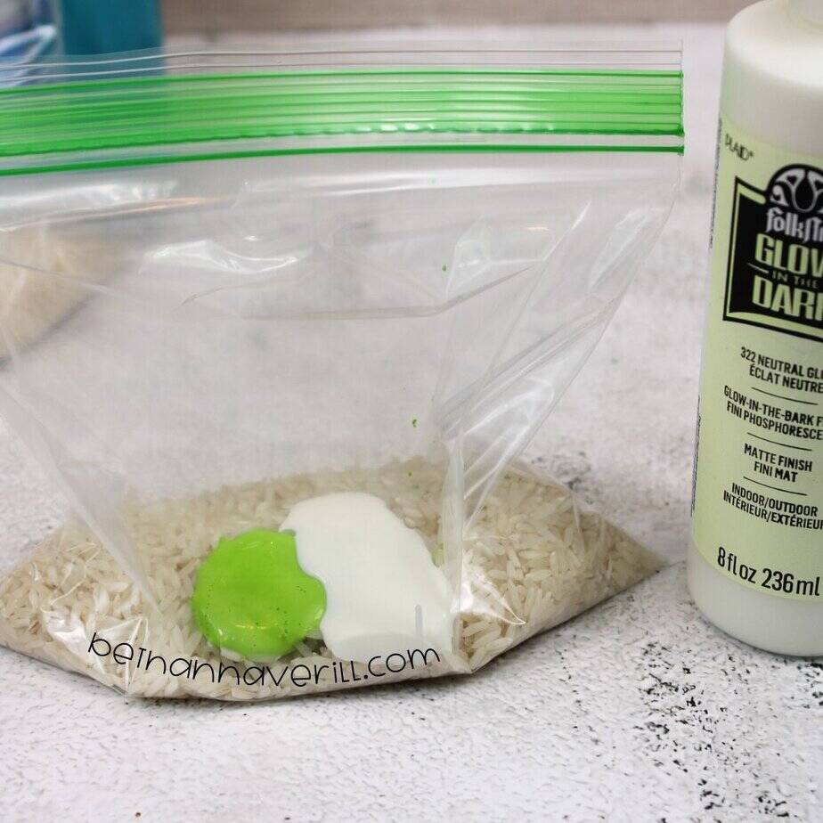 A zip-top bag of rice has both neon green paint and white glow-in-the-dark paint added on top, with the glow paint bottle visible beside it.