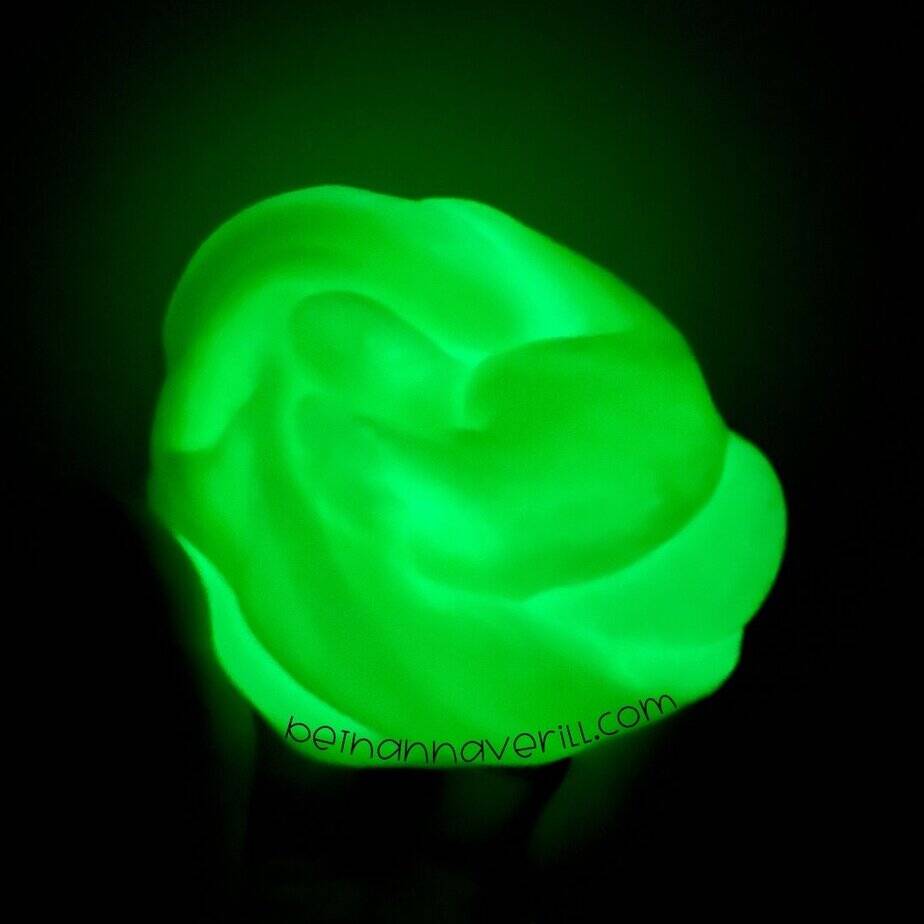 A luminous green glob of slime glowing in the dark, held in hand. The soft texture and bright glow are clearly visible.