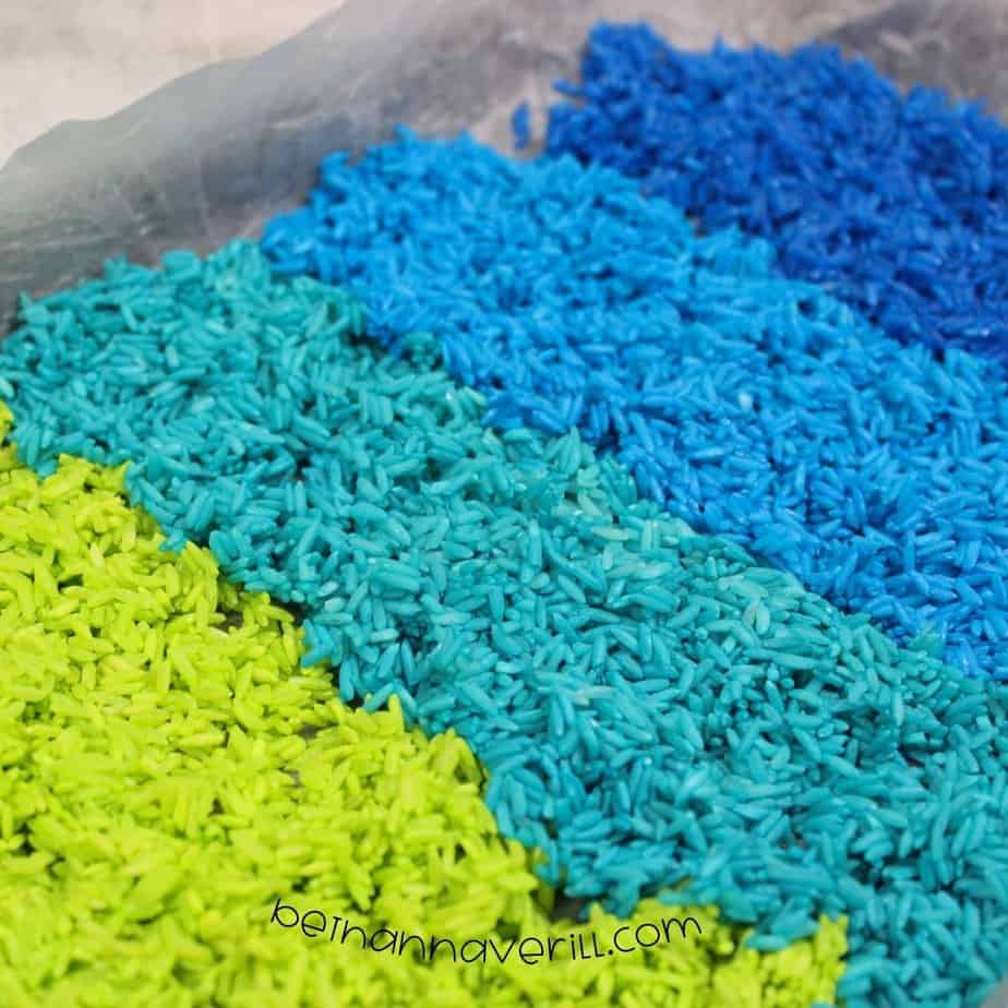 Close-up shot of dyed rice in vibrant stripes of green, teal, light blue, and dark blue laid out on parchment paper to dry.