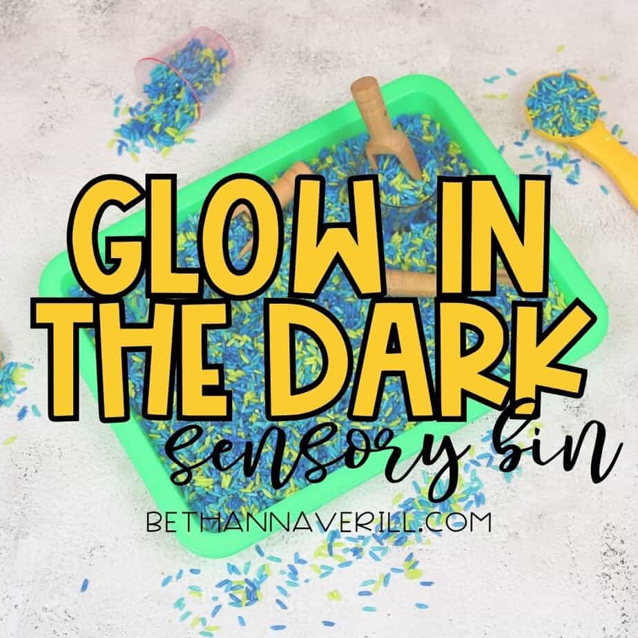 A green sensory bin filled with blue and yellow rice sits on a textured surface, surrounded by scattered rice and small scooping tools. Overlaid text reads “Glow in the Dark Sensory Bin” in bold yellow and black lettering, with the website bethannaverill.com below.