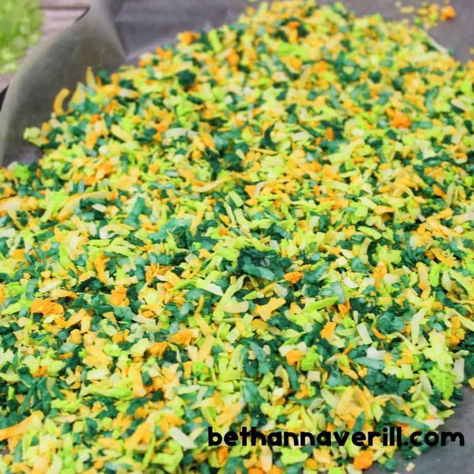 A vibrant pile of shredded coconut dyed in green, yellow, and orange hues spread across a baking tray. The texture mimics grass or leaves, perfect for a bug-themed sensory project.