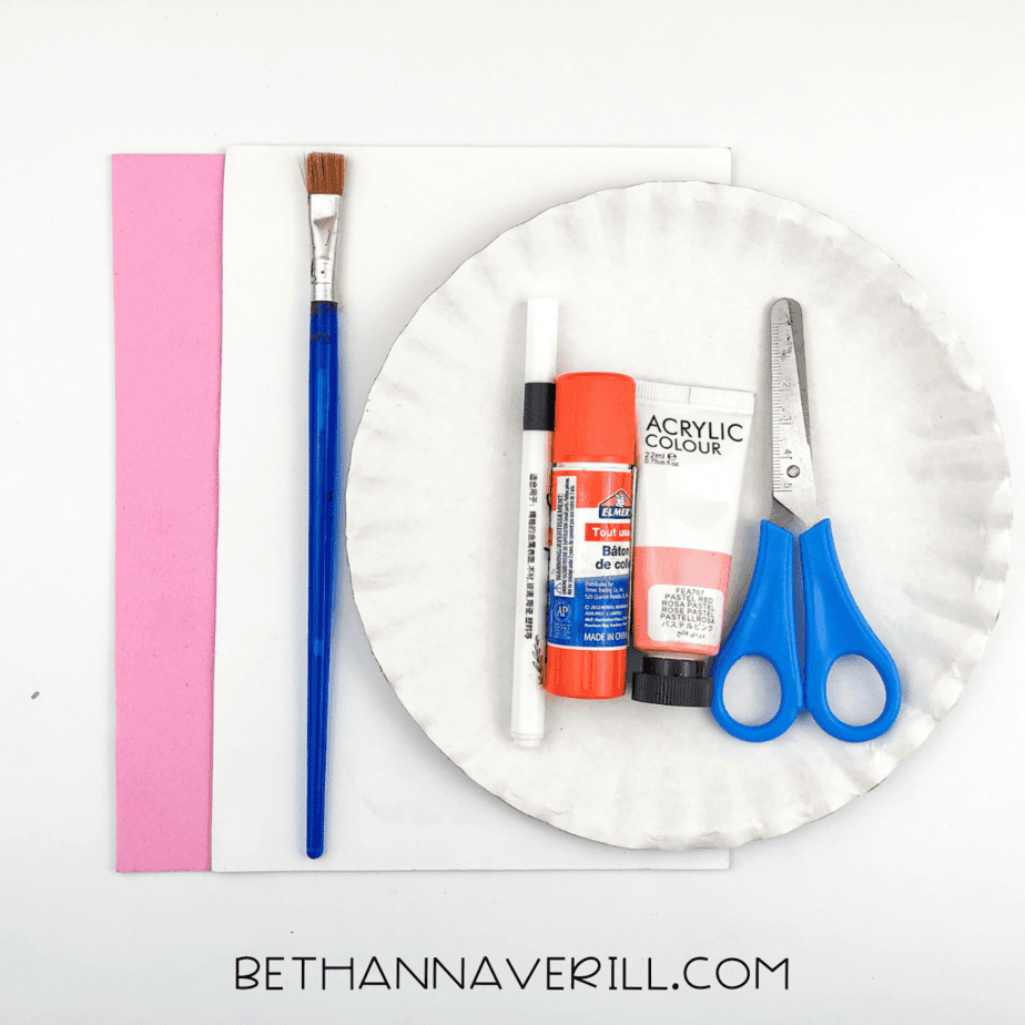 A flat lay of all the supplies needed for the flamingo craft, including pink and white paper, scissors, paint, glue, and a paintbrush.