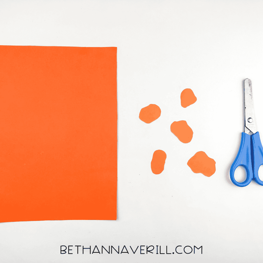 Orange construction paper cut into wiggly giraffe spots with scissors and paper nearby.