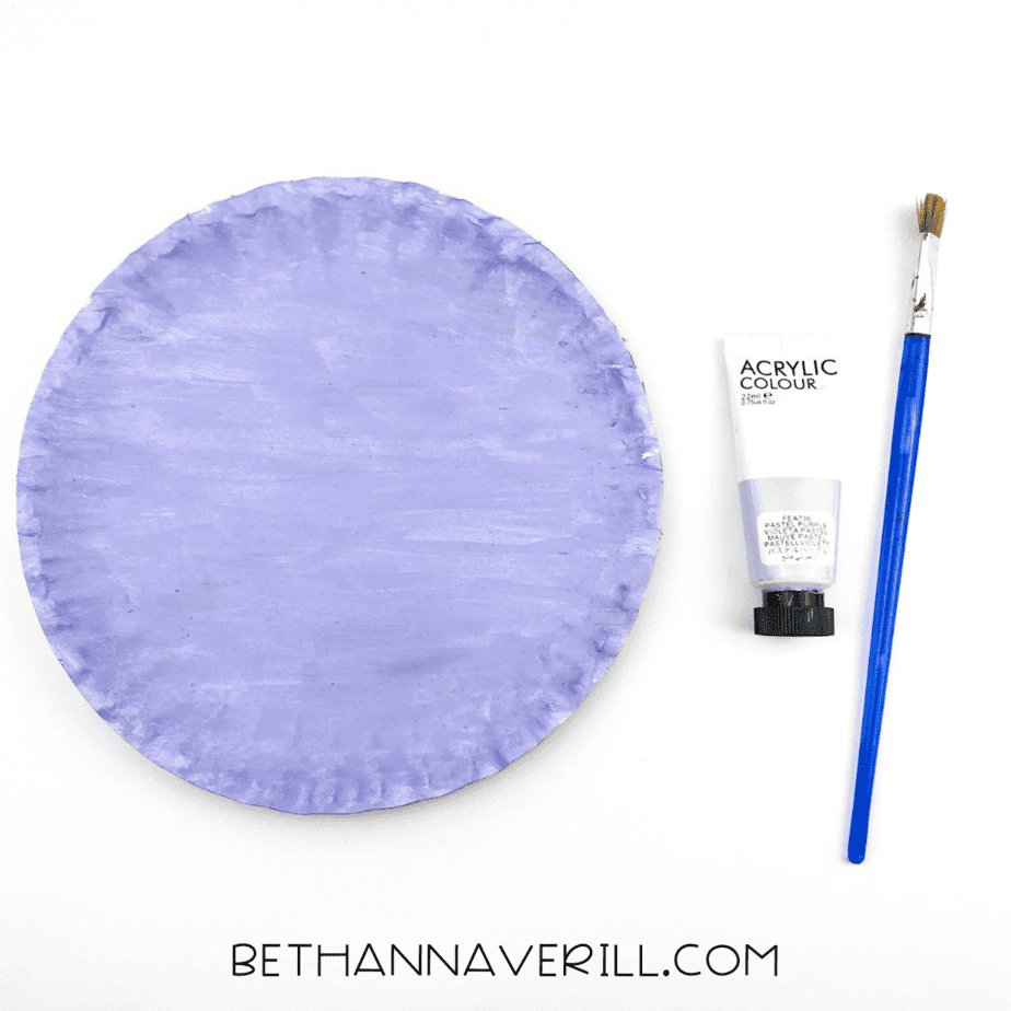 A paper plate painted purple with a brush and paint tube next to it.
