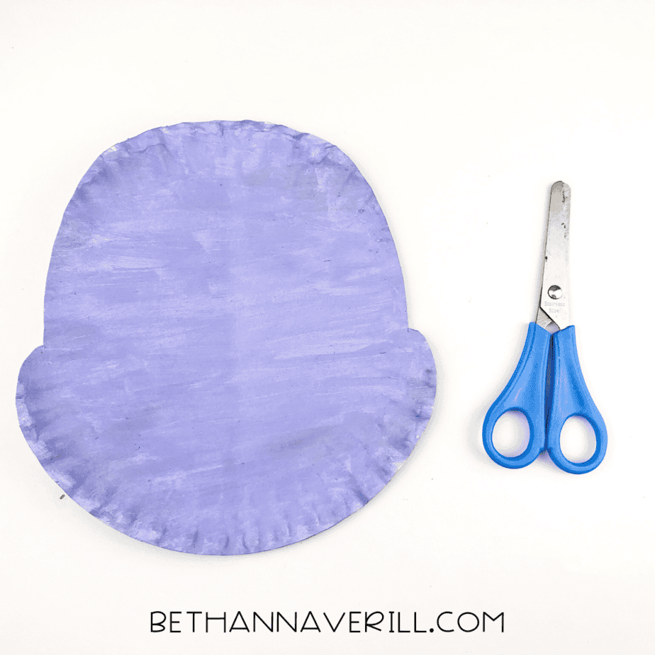 The purple-painted paper plate cut into the shape of a hippo's head with rounded cheek bumps.