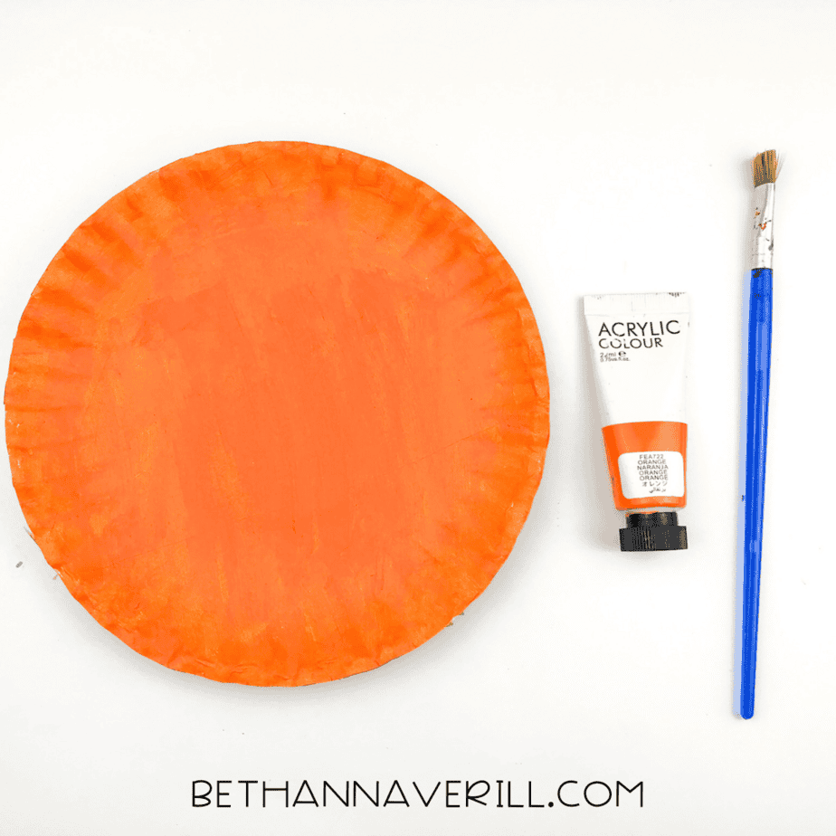 Paper plate painted entirely orange and drying next to the orange paint tube and brush