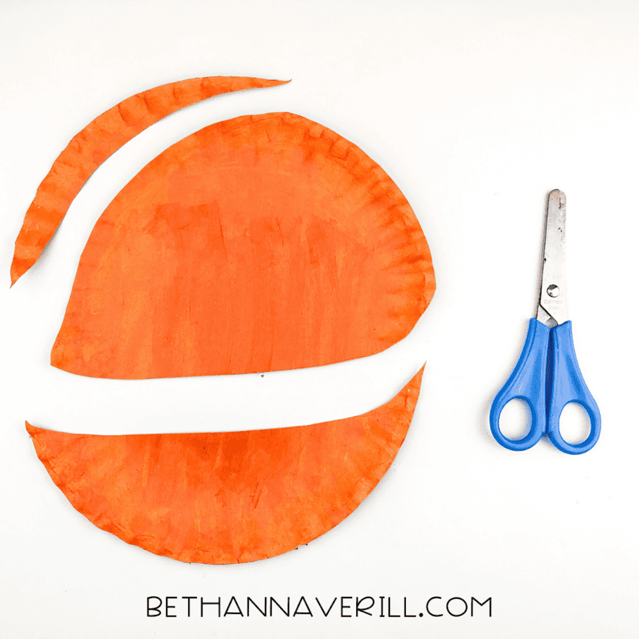 Orange painted paper plate cut into three shapes: a large head, a curved strip, and a skinny tail