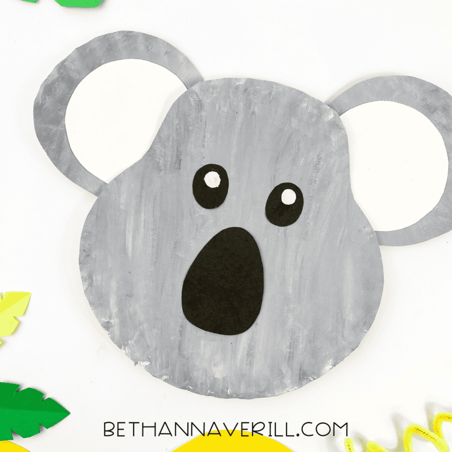Finished koala paper plate craft decorated and placed on a white surface with green paper leaves around it.