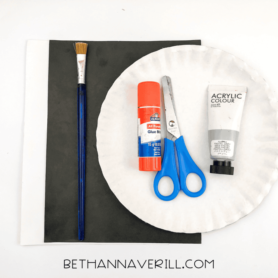 Supplies laid out for the koala paper plate craft, including two paper plates, glue stick, scissors, gray paint, paintbrush, and black and white paper.