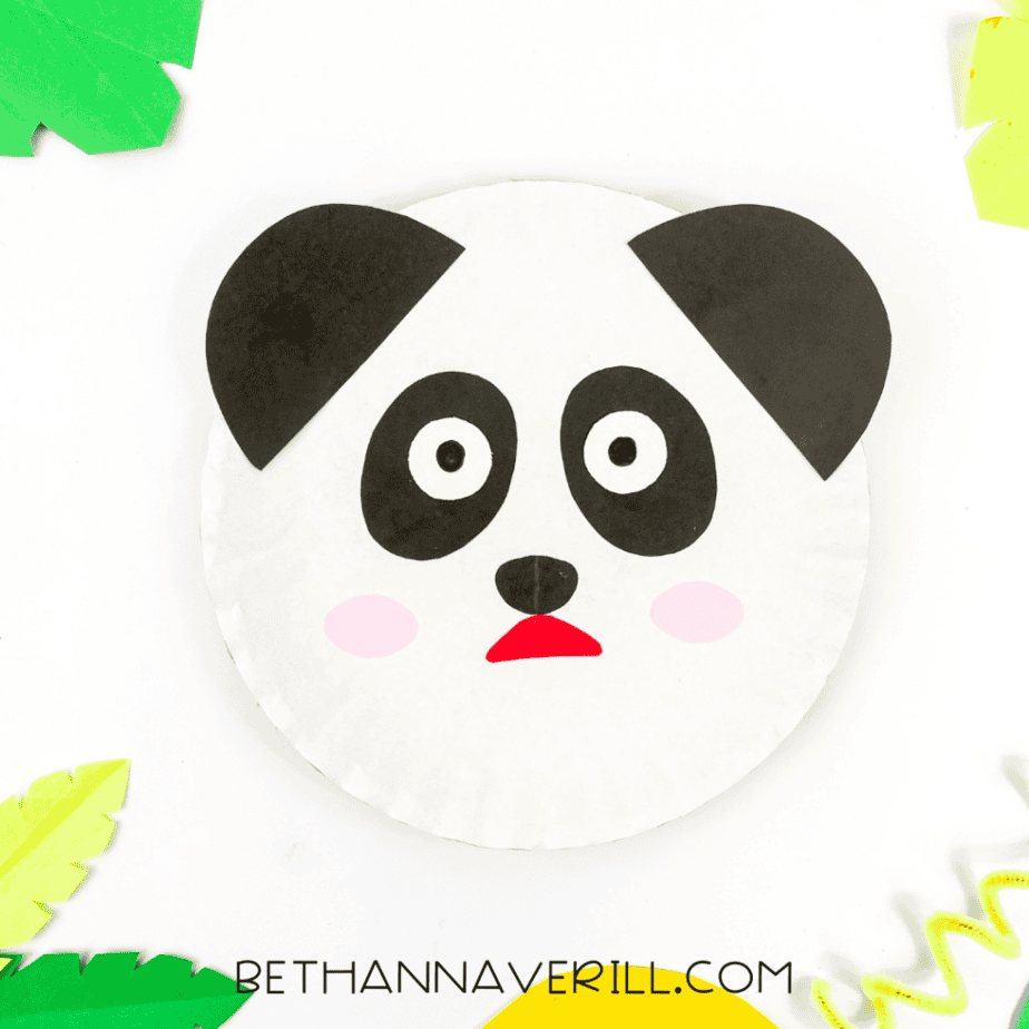 The completed panda paper plate craft displayed with colorful green leaves and yellow spiral accents.