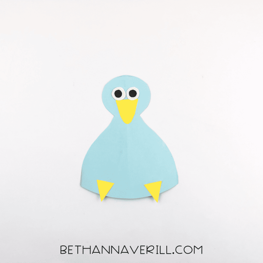 The blue paper peacock body now has paper eyes added above the beak, ready for its tail.
