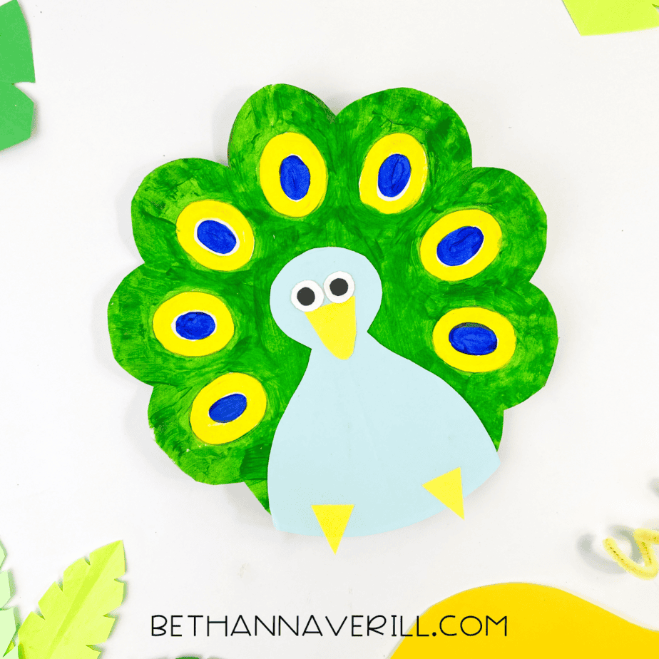The finished peacock paper plate craft displayed with paper leaves around it for a playful, tropical look.